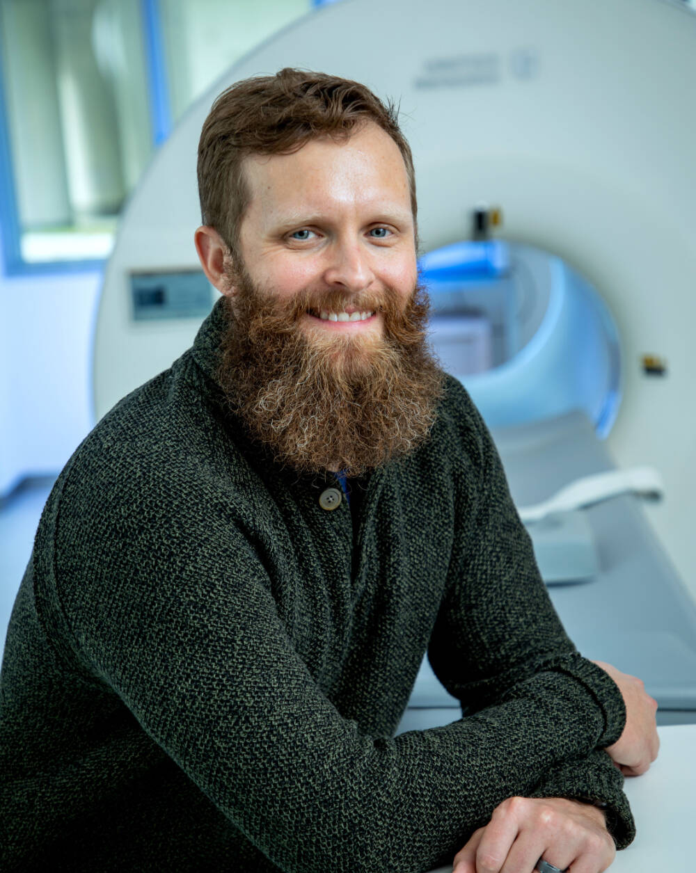 Kevin Maupin standing in front of a MRI machine leaning on it in a professional landscape.